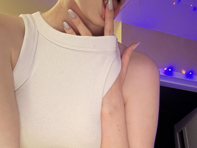SelinaRose's white ribbed tank top, showing her bare shoulder and upper chest, with her hand touching her neck, silver nail polish, and blue light in the background.