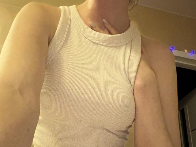 SelinaRose's white ribbed tank top shows her small, perky tits and a tattoo on her neck. Her right arm is slightly raised. Her skin is light.