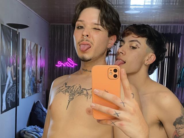 AronJames with tattoos, sticking out tongue, has a nose ring and black hair, holds an orange phone, another AronJames with black hair and eyeliner licks his ear.