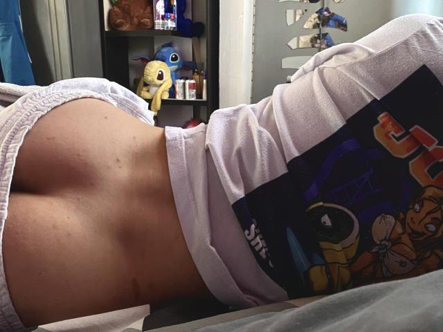 AronJames lying on their side, showing a bare, tan-skinned ass in white underwear, with a colorful shirt and a toy Pikachu in the background.