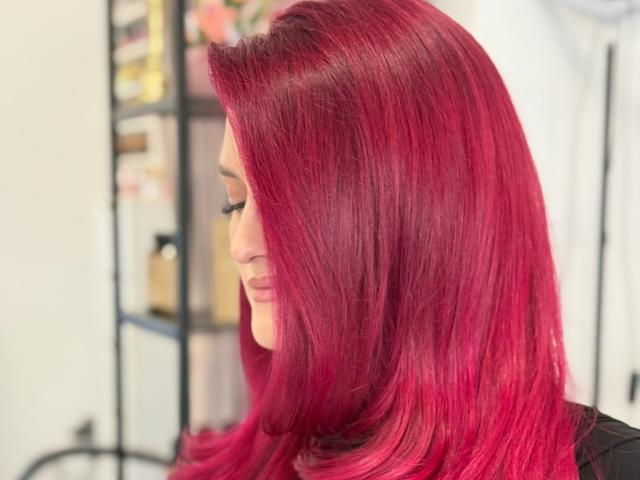 Rosalyn mit glänzendem, leuchtend rosa Haar, die nach unten schaut und schwarze Kleidung trägt, in einem gut beleuchteten Innenraum, die ihr glattes, langes und glänzendes Haar zur Schau stellt..