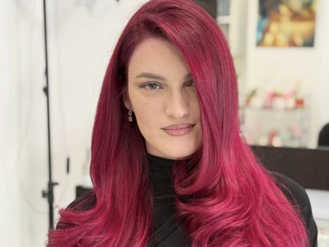 Rosalyn mit leuchtend rosa Haaren, einem schwarzen Rollkragenpullover und dezentem Make-up zwinkert in die Kamera. Sie hat einen sexy, selbstbewussten Look und ein süßes, symmetrisches Gesicht..