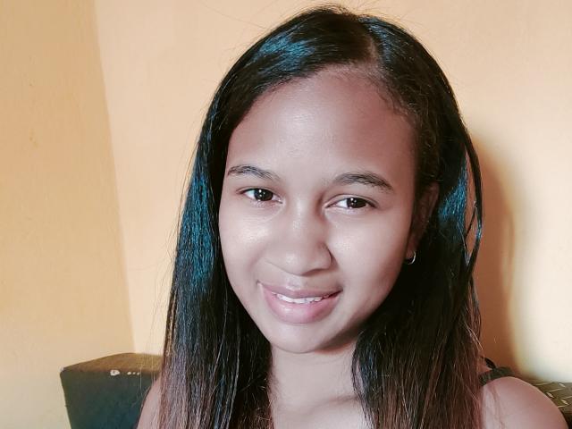 LoderFist has smooth brown skin, long black hair with blue highlights, small brown eyes, and a subtle smile, wearing a tiny black earring, showing her cute, shiny tits.