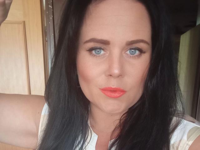 HerrinLana-hot has pale skin, blue eyes, black hair, and bright orange lipstick. Her tits are not visible. She's making a pouty face, looking directly at the camera.
