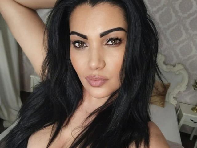 BeliseChappelleX-hot has long black hair, brown eyes, and is wearing a black top, looking at the camera with a slight smile, showing her nose and full lips.