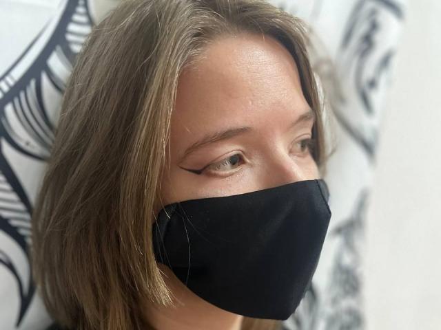 A photo of sweetbasil with light brown hair, wearing a black mask, showing off sharp eyeliner and slightly sweaty forehead. Her eyes are looking to the side.