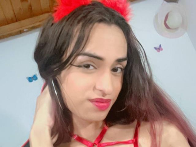 AngieTsSex with dark brown hair, red lipstick, and red furry headpiece, wearing red lingerie, has a nose ring, and is looking at the camera with a slight smile.