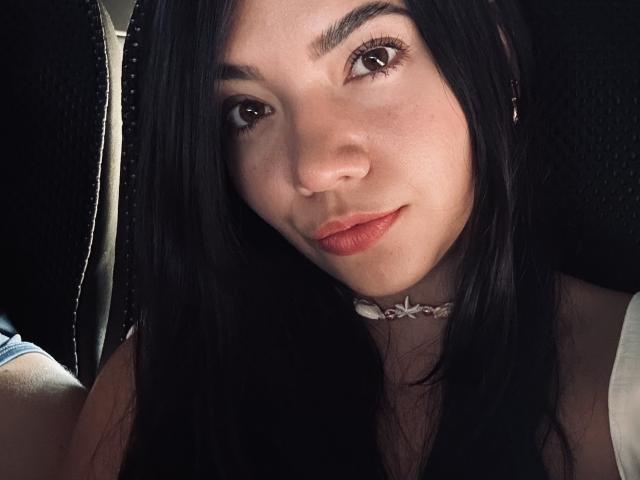 SofieWhite has black hair, brown eyes, and a subtle smile with red lipstick. She's wearing a white choker and a sleeveless top, with a slight nose freckle.