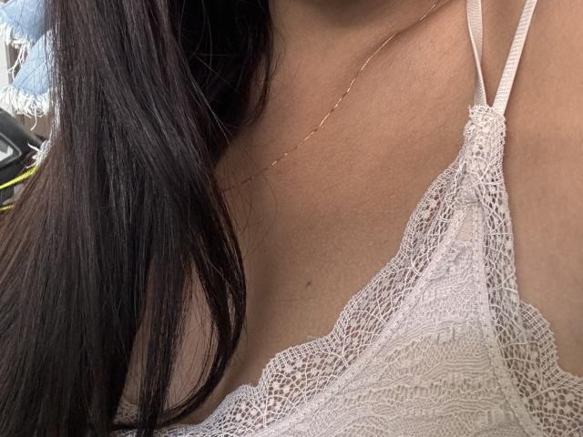 SofieWhite's tits in a white lace bra, showing a delicate, intricate pattern. Her long, dark hair is partially visible on the left side. She's wearing a thin gold necklace.