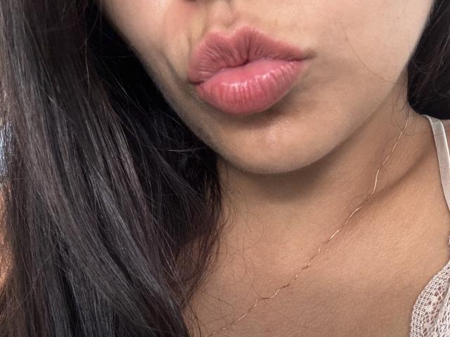 SofieWhite's plump, pinkish-red lips are slightly pouted. She has long, dark brown hair and is wearing a thin, gold necklace. Her tan skin is visible.