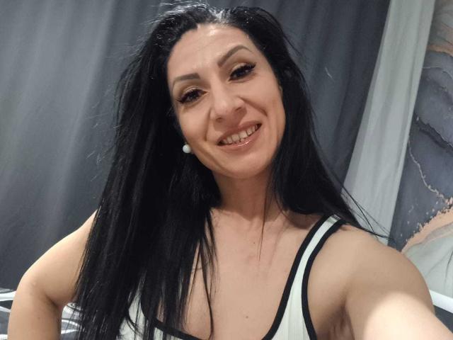 LanceDance, con lunghi capelli neri, sorridente, indossa una canotta bianca con bordi neri, che mostra il seno, e porta un orecchino di perle, in un selfie..