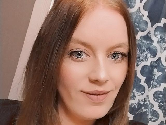 DollySoumise69 has light brown hair, blue eyes, and a slight smile. She's looking at the camera with her eyebrows slightly raised. Her makeup is subtle and natural.