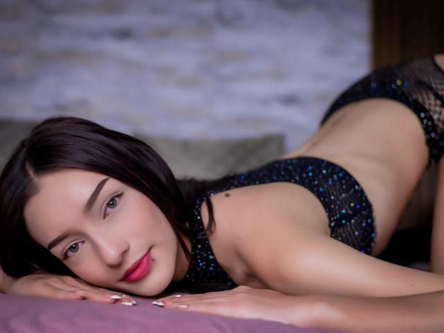 AliceBakerr is on her knees, face down, with her ass up, wearing a sparkly black bra and panties, black hair, pink lip, and a subtle nose piercing.