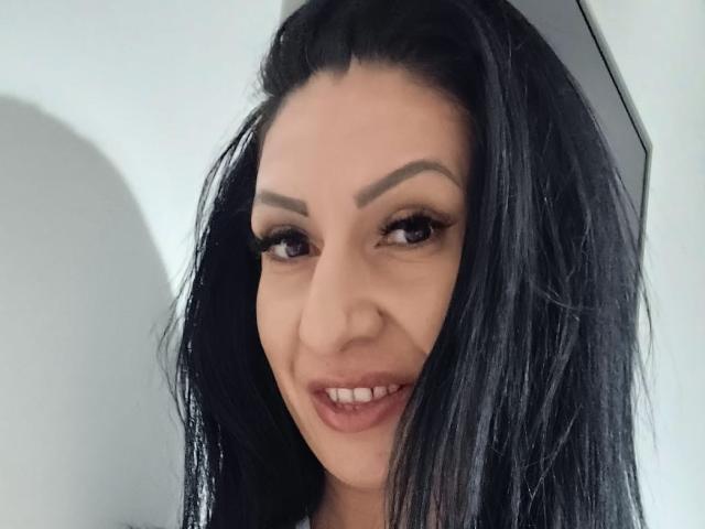LanceDance heeft zwart haar, dikke wenkbrauwen en ze glimlacht met haar lippen lichtjes open, waardoor haar tanden zichtbaar zijn. Haar ogen zijn donker en ze kijkt naar de camera..