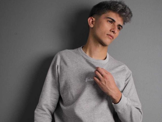 CandyEngel, with short gray curly hair, wearing a gray sweatshirt, holds the collar with one hand, looking off to the side with a slight smirk.