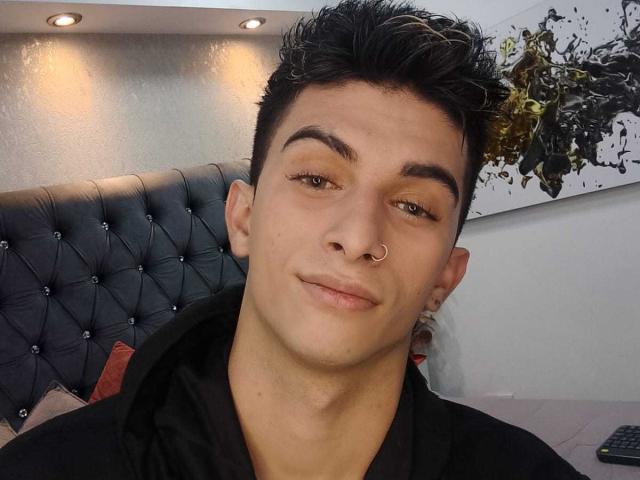 CandyEngel has short, dark, spiked hair, a nose ring, and a slight smile. CandyEngel's eyebrows are thick, and he's wearing a black shirt.