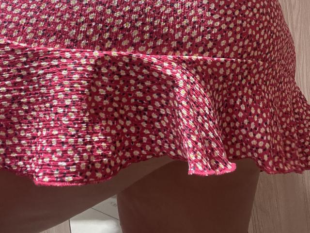 La falda floral rosa y blanca de Barbarica está acampanada, mostrando su trasero desnudo y la parte superior de sus muslos. La tela está ligeramente arrugada, y la falda está levantada..