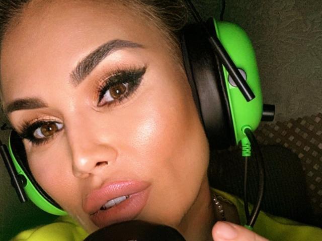 RadmilaQueen with tan skin, brown eyes, and full pink lips, wearing green and black headphones, has thick eyebrows, and long eyelashes, looking at the camera with a slight smile.