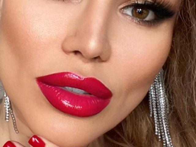 RadmilaQueen's face, featuring glossy red lipstick, long eyelashes, brown eyes, and silver dangling earrings, with a close-up focus on her lips and upper facial features.