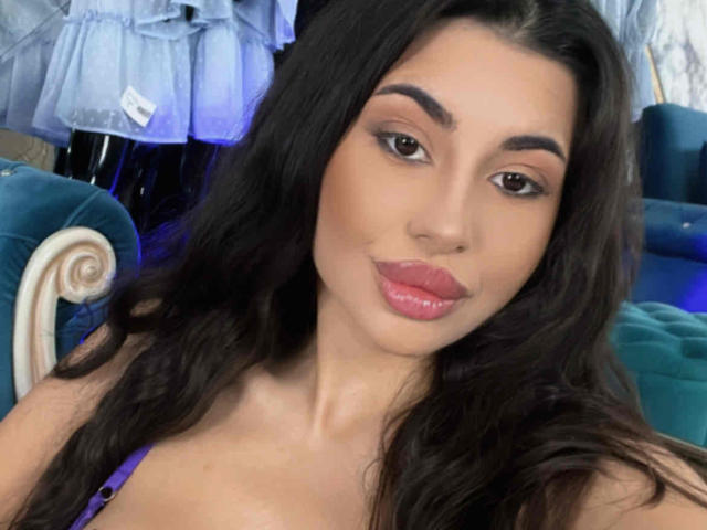 LatinaLoco has long dark hair, brown eyes, and glossy pink lips, wearing a purple top, with a cute, sexy face and subtle makeup.