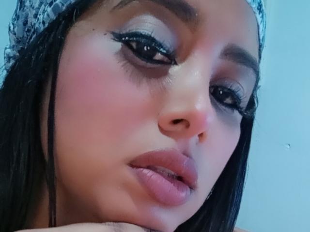 MariaCatalina's face with pink blush, long eyelashes, and full pink lips, wearing a patterned headscarf, looking slightly to the side with a subtle, sexy, sultry expression.