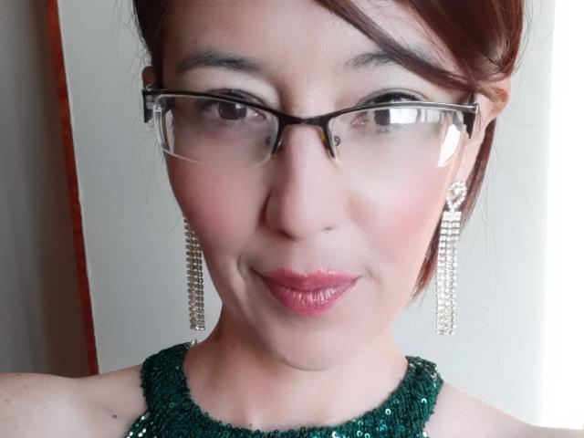 AntonnellaS has glasses, green sequined dress, and chandelier earrings. She's smiling with pink lipstick, and her brown hair is up. Her tits are small and her pussy is unseen.