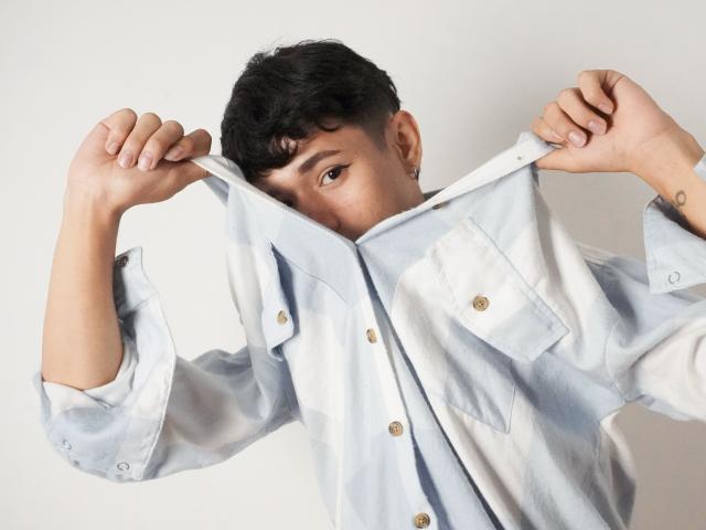 DanteEvans with short curly black hair, wearing a light blue and white striped shirt, pulling it up to show his face and brown buttoned pockets. Hands gripping shirt edges.