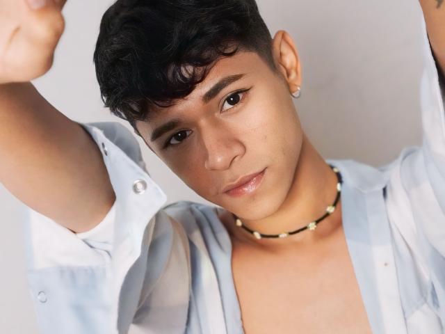 DanteEvans has short, curly black hair, a nose piercing, and a cute face with a subtle smile. Wearing a blue-striped shirt and a black bead necklace.