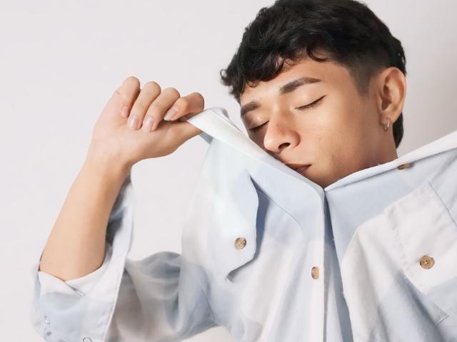 DanteEvans, with short curly black hair and light brown skin, is sleeping with eyes closed, wearing a light blue button-up shirt, pulling it slightly over his face.