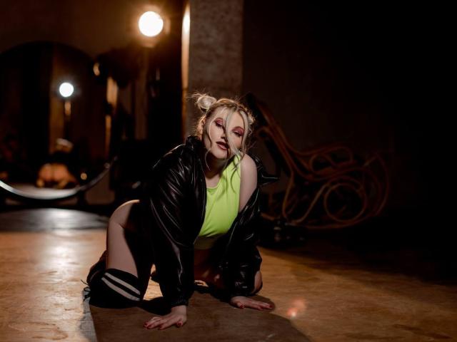 AshleyJonse op handen en voeten, met een felgroene top, een zwarte leren jas en kniekousen, met een donkere, sfeervolle achtergrond, gloeiende lichtbronnen en een melancholische uitdrukking..
