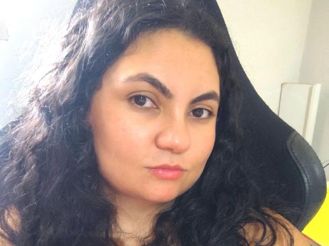 Marymanroe has curly black hair, brown eyes, and pink glossy lips, sitting in a black chair, looking directly at the camera with a slightly pouty expression.