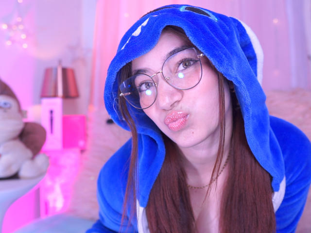 IssaMonterrey with glasses, pouty pink lips, and blue Pokémon hoodie, her brown hair down, blue eyes, and fair skin, looking cute in a purple-lit room.