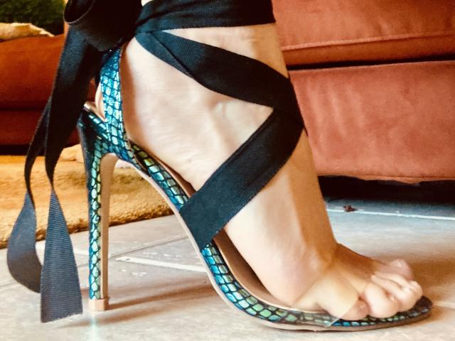 MagdaMedusa's foot in a high-heeled sandal with blue and green patterned fabric and black ribbon straps, her toes curled, showing her sole and the heel's metallic stiletto.