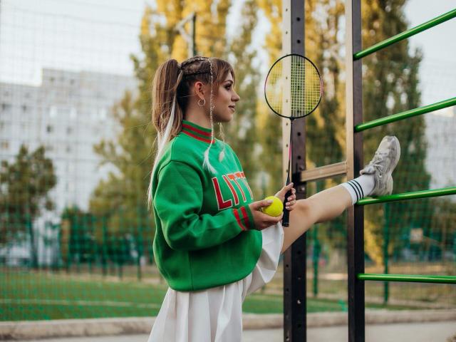 DreamySamantha with long brown hair in a green and red sports sweater, white skirt, holding a yellow tennis ball, raising her leg on a green ladder, holding a racket.