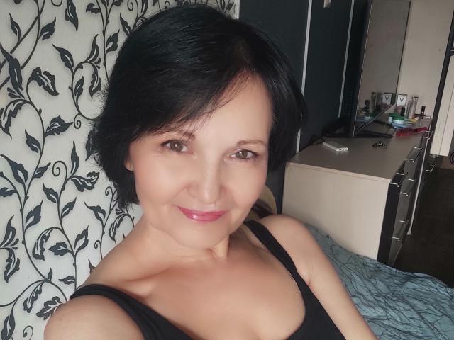 KetiLoverX with short black hair, brown eyes, and pink glossy lips, smiling at the camera, wearing a black tank top, showing small tits and a cute face.