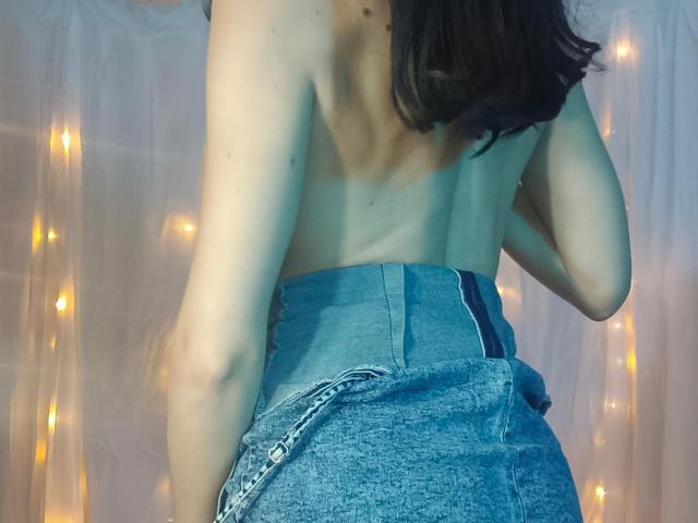 OrianaLaFrancaise's bare back, wearing high-waisted blue jeans, her hand on her butt, dark wavy hair, soft yellow fairy lights in the background.