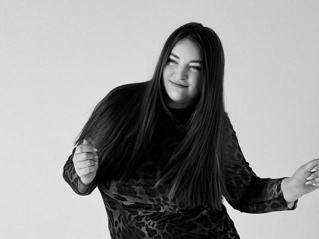 NataliePeterson has long dark hair, wearing a black leopard print dress, smiling with eyes slightly closed, fists raised, right arm bent, left arm extended, in a black-and-white photo.