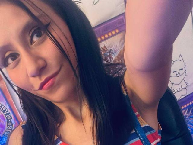 EviieGothel with black eyeliner, pink lips, and straight dark hair, raising her arm, wearing a colorful patterned top, showing her small tits and cute face.