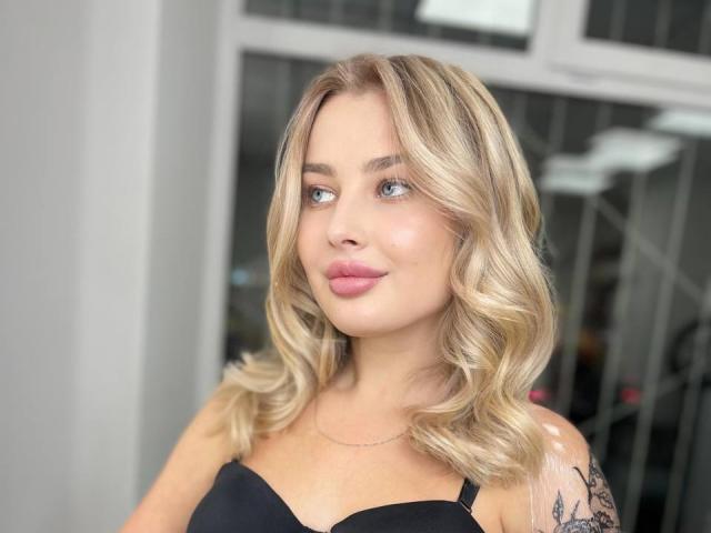 PolinaLaur heeft blond, golvend haar, blauwe ogen en roze lippen, en draagt een zwarte bh, met een tatoeage op haar rechter schouder. Ze kijkt opzij met een lichte glimlach..