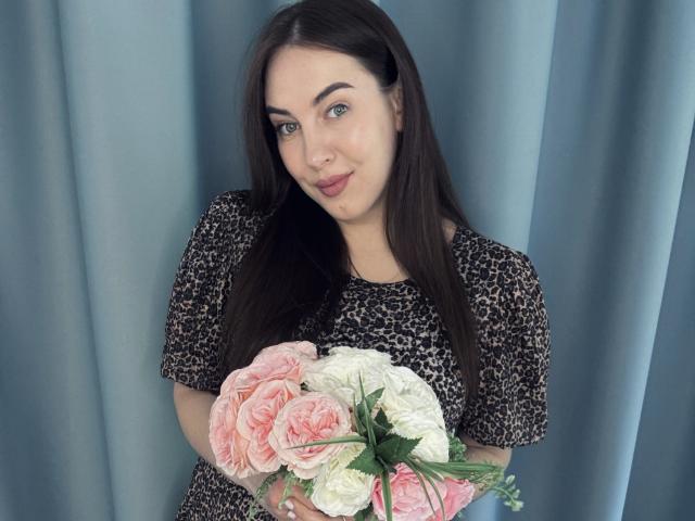 KaleyReed with long brown hair, blue eyes, and a nose ring, wearing a leopard print shirt, holding a pink and white rose bouquet in front of her.