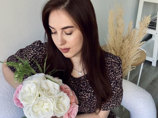 KaleyReed with long brown hair, wearing a leopard print top, holding a bouquet of white and pink roses, looking down, sitting on a white chair, puffy pinkish tits.
