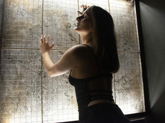 MichelleHotX69 with side profile, hands on window, wearing black sparkly dress, back cutout, medium tits, blonde hair, sunlit, smiling, standing, mid-action, sexy.