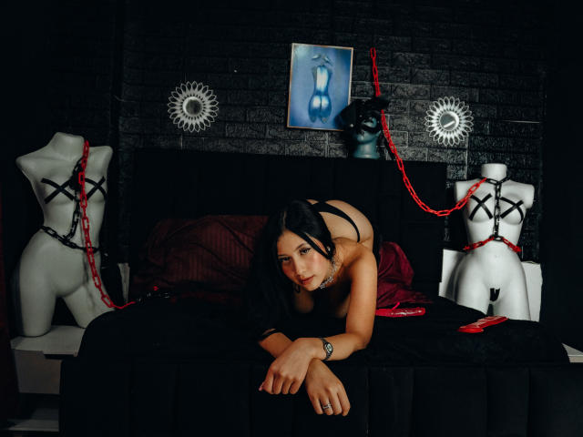 EmmaKimura, black-haired, on black bed, black lingerie, butt up, arms forward, red rope on white mannequins, black brick wall, dark room, looking at camera, sexy, BDSM.