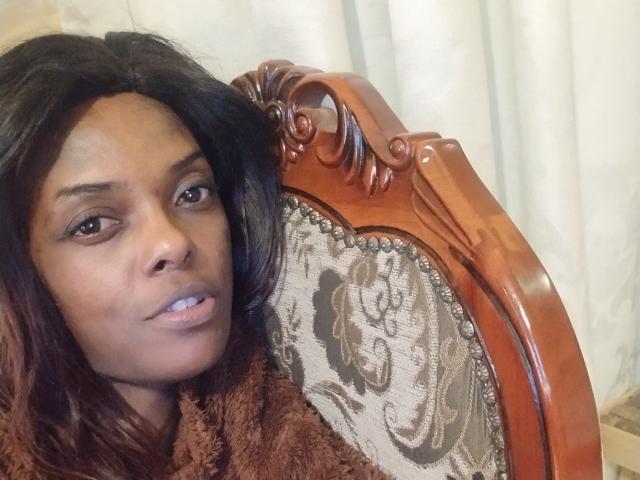 LeaStar with brown hair, medium skin, and small tits, leaning on a fancy wooden chair with floral upholstery, wearing a brown fuzzy sweater, looking slightly confused.