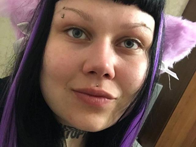 BetsiBlum a la peau pâle, les yeux bleus, les cheveux noirs et violets, des oreilles de chat et un piercing au nez. Elle a l'air boudeuse, avec un petit anneau dans la lèvre et un tatouage au cou..