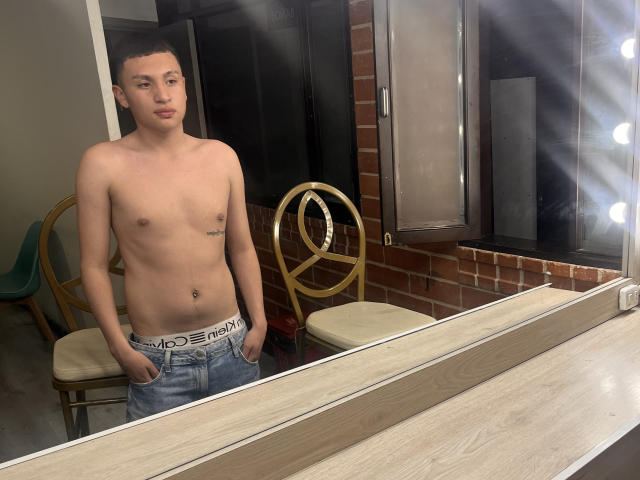 Shirtless AronSweety with short brown hair, light skin, and a small tattoo on the right side of his chest, wearing blue jeans and white Calvin Klein underwear, standing in front.