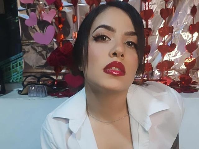 MelisaLeon con le labbra rosse lucide, i capelli scuri raccolti in uno chignon, indossa una camicia bianca, guarda leggermente verso l'alto, ha una collana e, sullo sfondo, c'è un cesto verde..