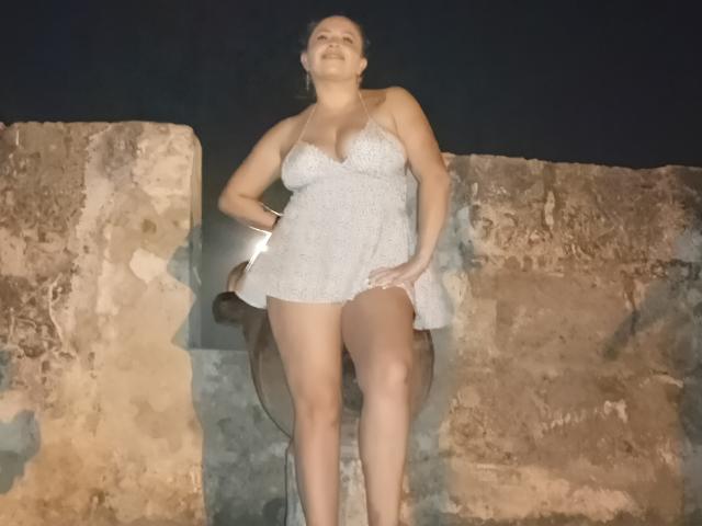FantasykLadies with large boobs, wearing a white, see-through dress, standing against a stone wall at night, looking confident, hand on hip, legs apart, dark background.