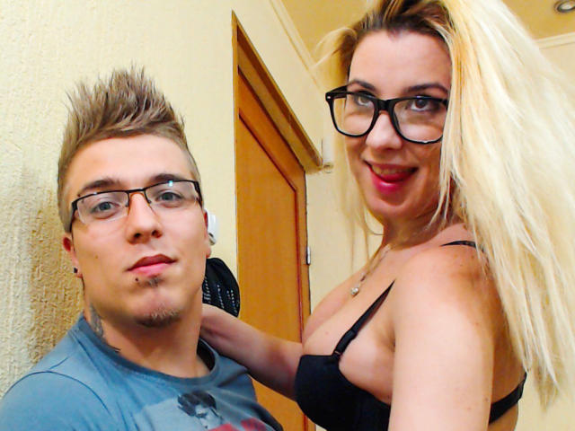BranlePourNous, avec des lunettes et des cheveux bruns hérissés, portant une chemise bleue, se tient à côté de BranlePourNous, avec des cheveux blonds, un soutien-gorge noir, montrant ses seins, souriant, et portant des lunettes..