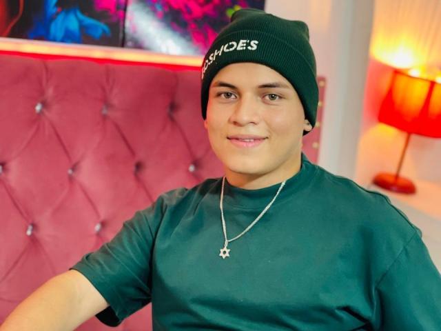 LeonAdams, wearing a green beanie and green shirt, with a cross necklace, smiling at the camera, has a cute face and a relaxed, confident vibe.